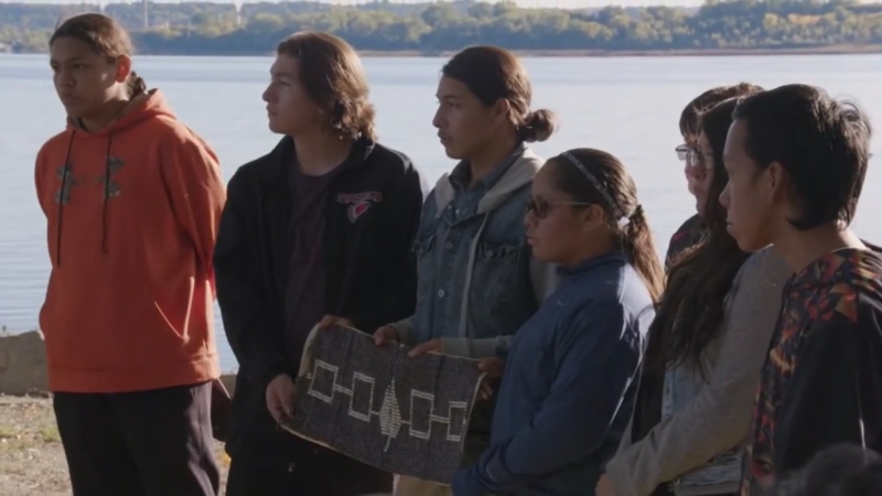 Iroquois youth stand by the water holding a wampum belt symbolizing their unity today