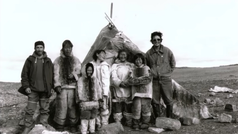 A group of Inuit people in traditional Arctic clothing made of fur and hide standing beside a shelter